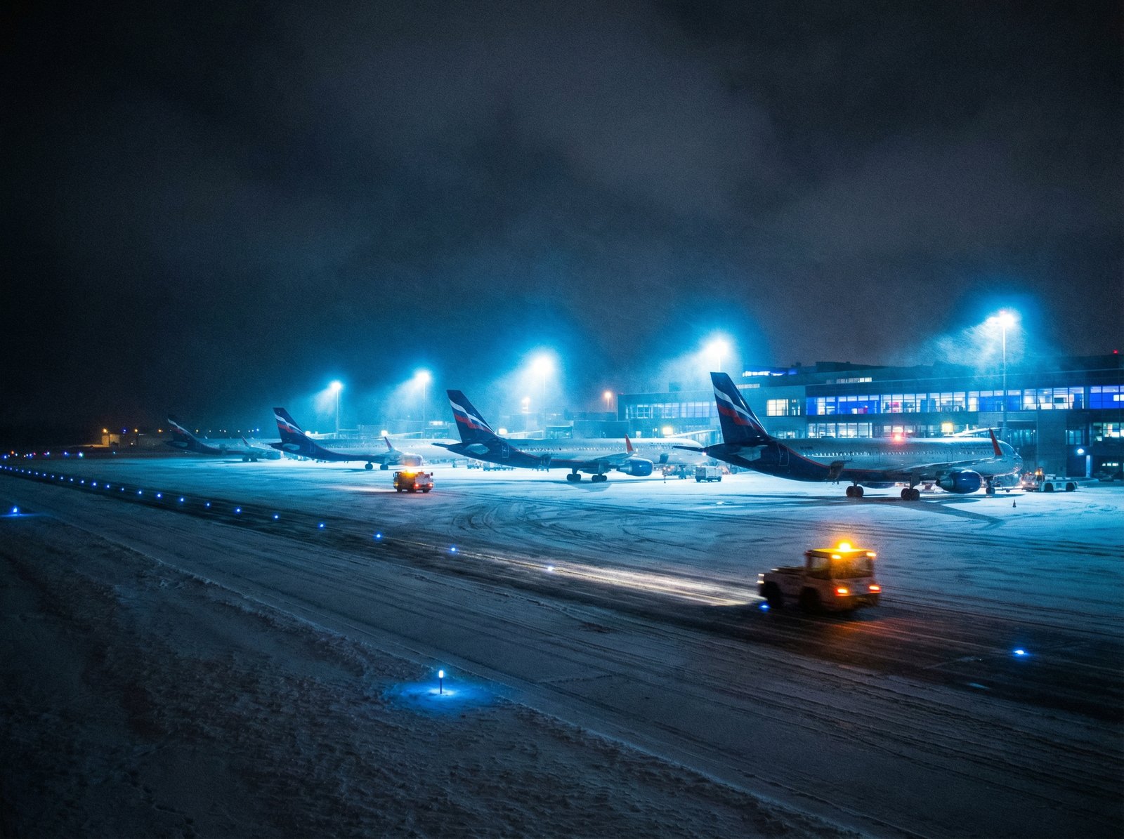 airplanes parked on a snowy runway at night with bright airport lights cinematic composition blue and white colors 4:3 aspect ratio no text