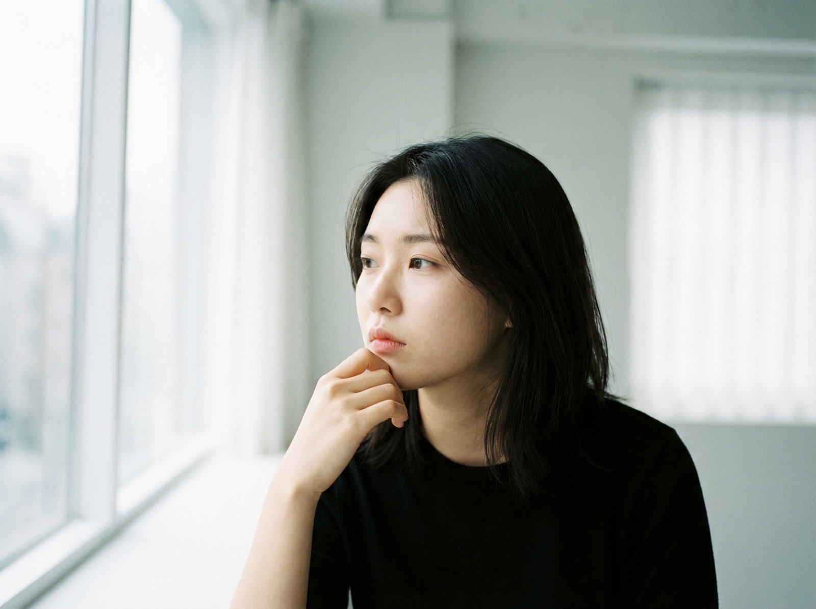 A thoughtful young woman with Korean features, looking into the distance with a pensive expression, considering deep questions. Soft, diffuse natural light, clean background, no visible text. Aspect ratio 4:3.