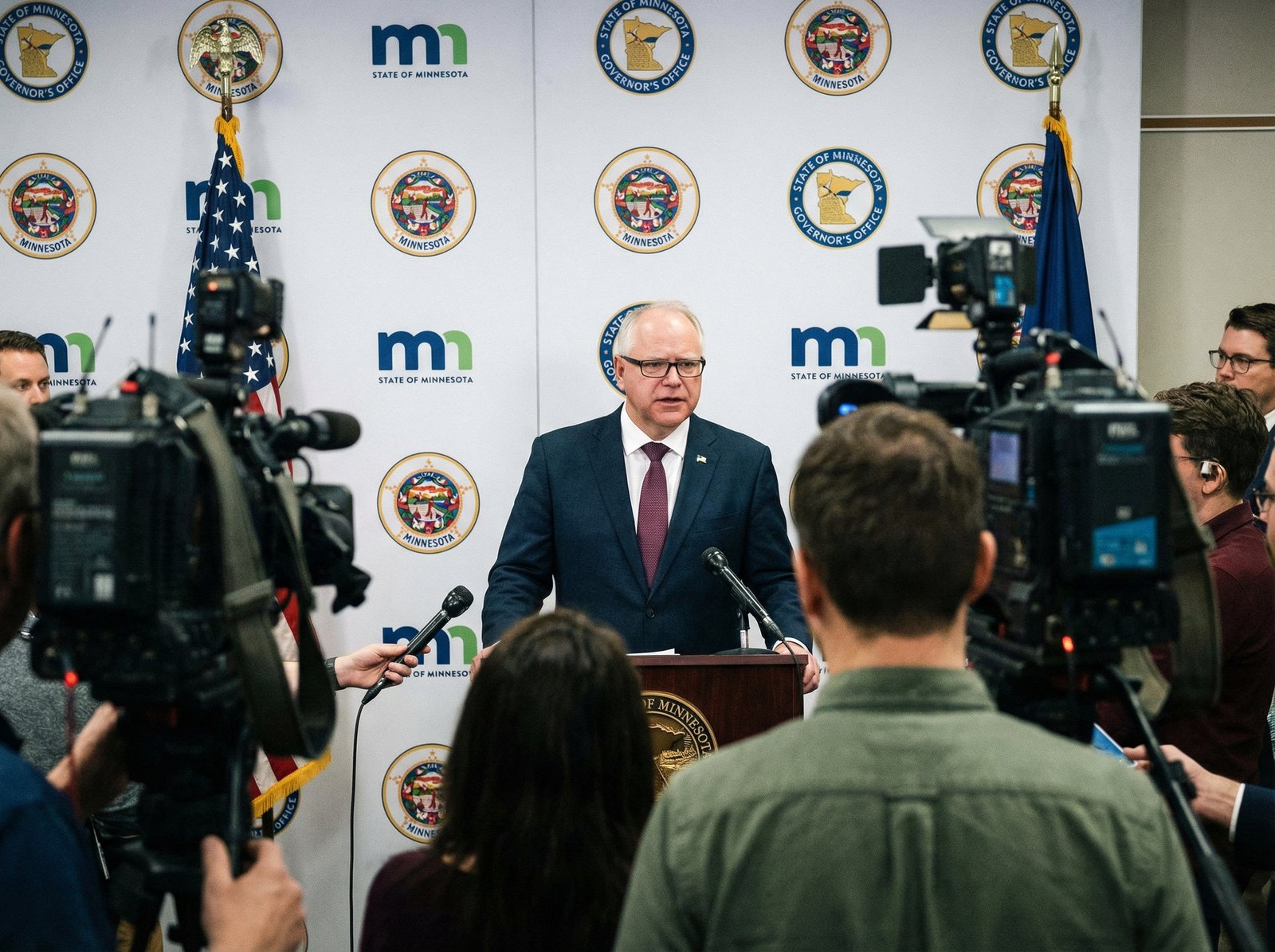 Minnesota Governor Tim Walz giving a press conference, looking serious and addressing the public. The background shows government seals. Aspect ratio 4:3, no visible text.