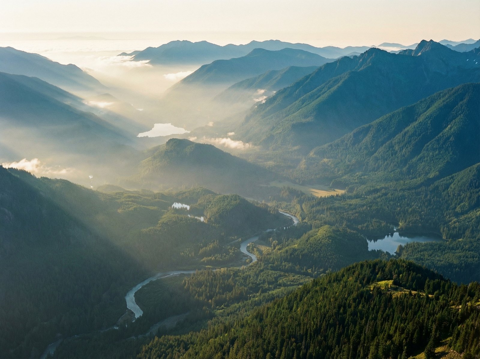 A breathtaking panoramic view of Olympic National Park mountains shrouded in morning mist, layers of blue and green ridges, pristine wilderness, wide angle, 4:3, cinematic lighting, natural colors, high resolution, no text.