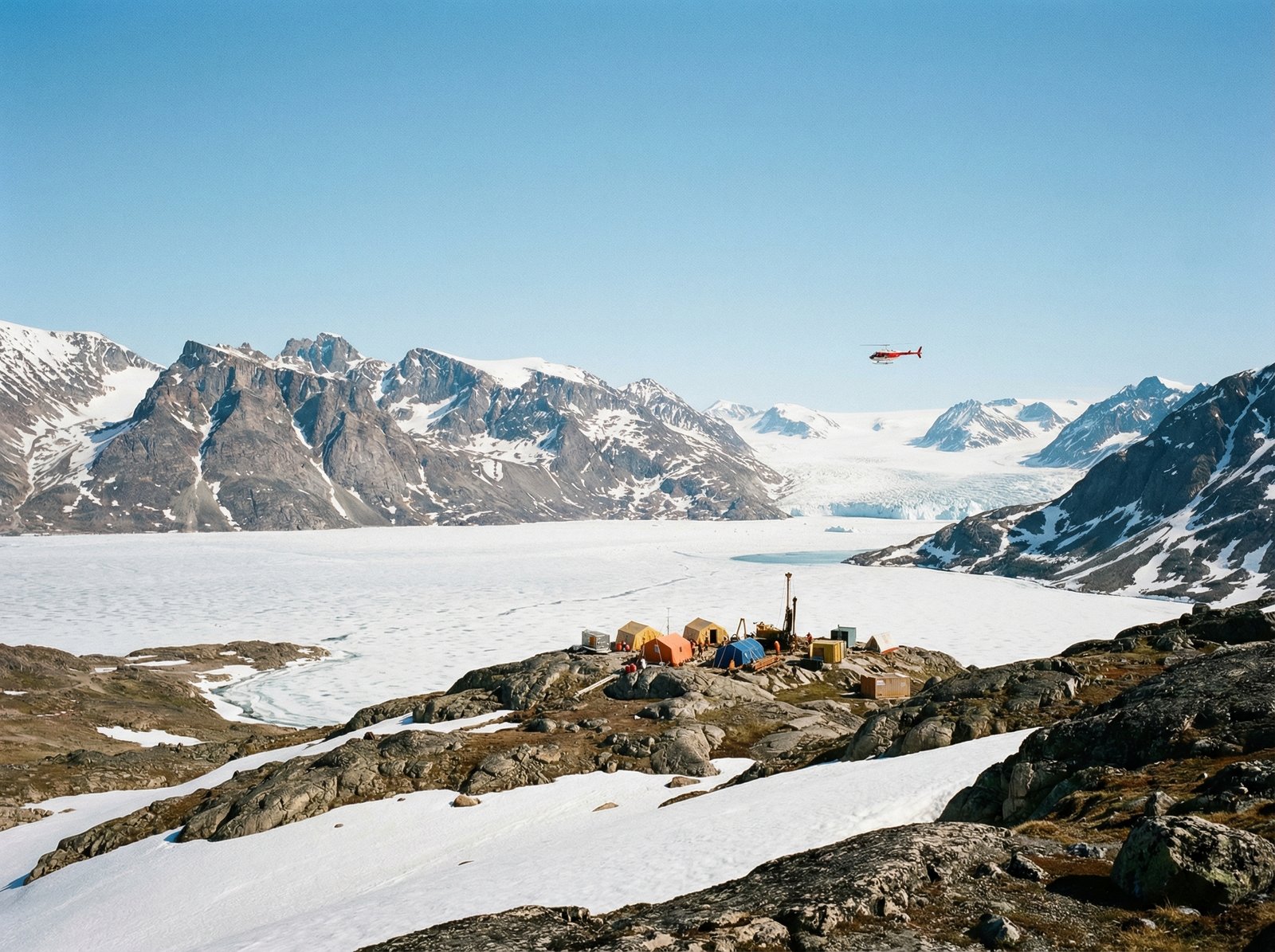 A wide-angle landscape of Greenland's snowy fjords and rocky mountains under a clear blue sky, featuring subtle mining exploration equipment and a helicopter in the distance, realistic cinematic photography, 4:3 aspect ratio, no text