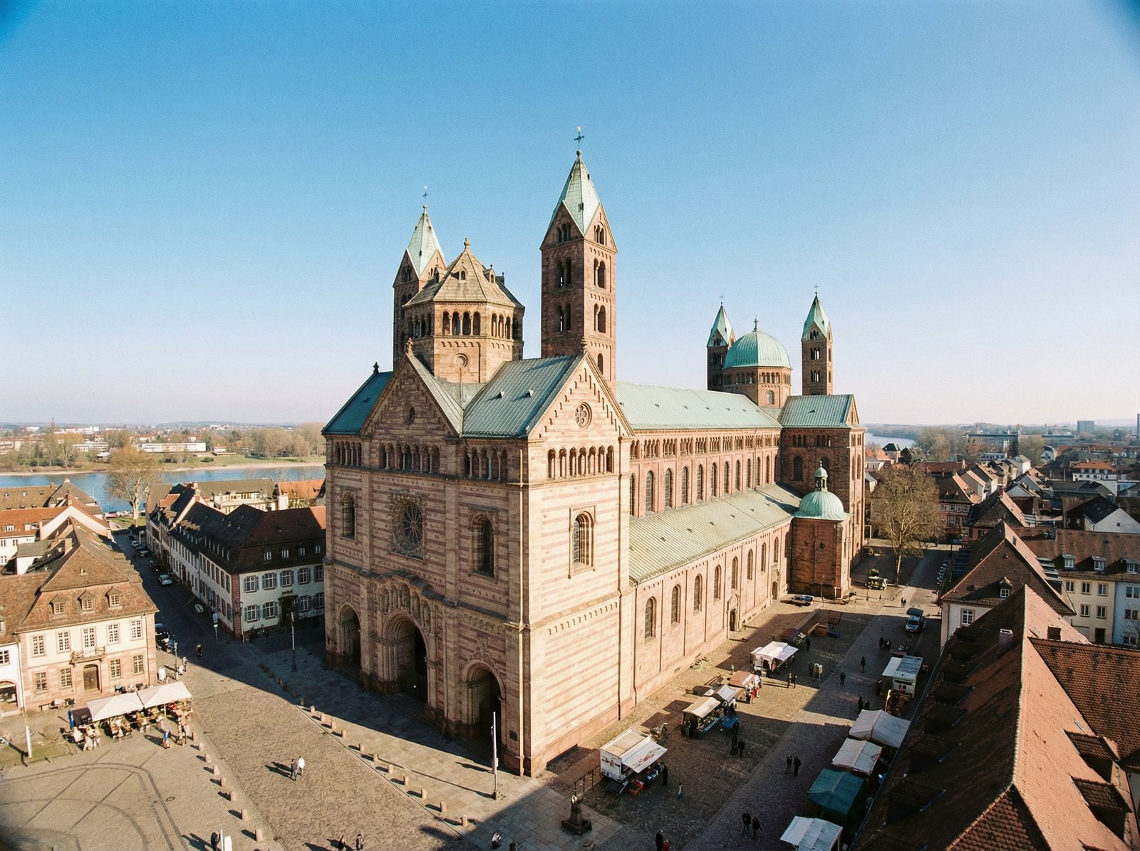 A grand wide-angle view of the Speyer Cathedral in Germany, showing its massive Romanesque structure built with red sandstone under a clear blue sky, majestic towers and domes, historic European city square background, high quality photography, 4:3
