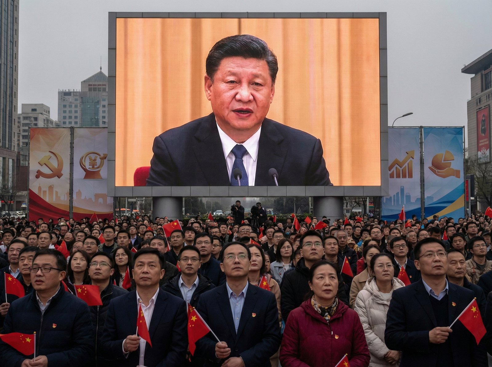 Chinese President Xi Jinping on a large screen at a public gathering, delivering a speech about economic policy. People are gathered, looking up at the screen. The scene has a sense of national focus and economic importance. Aspect ratio 4:3, no visible text.