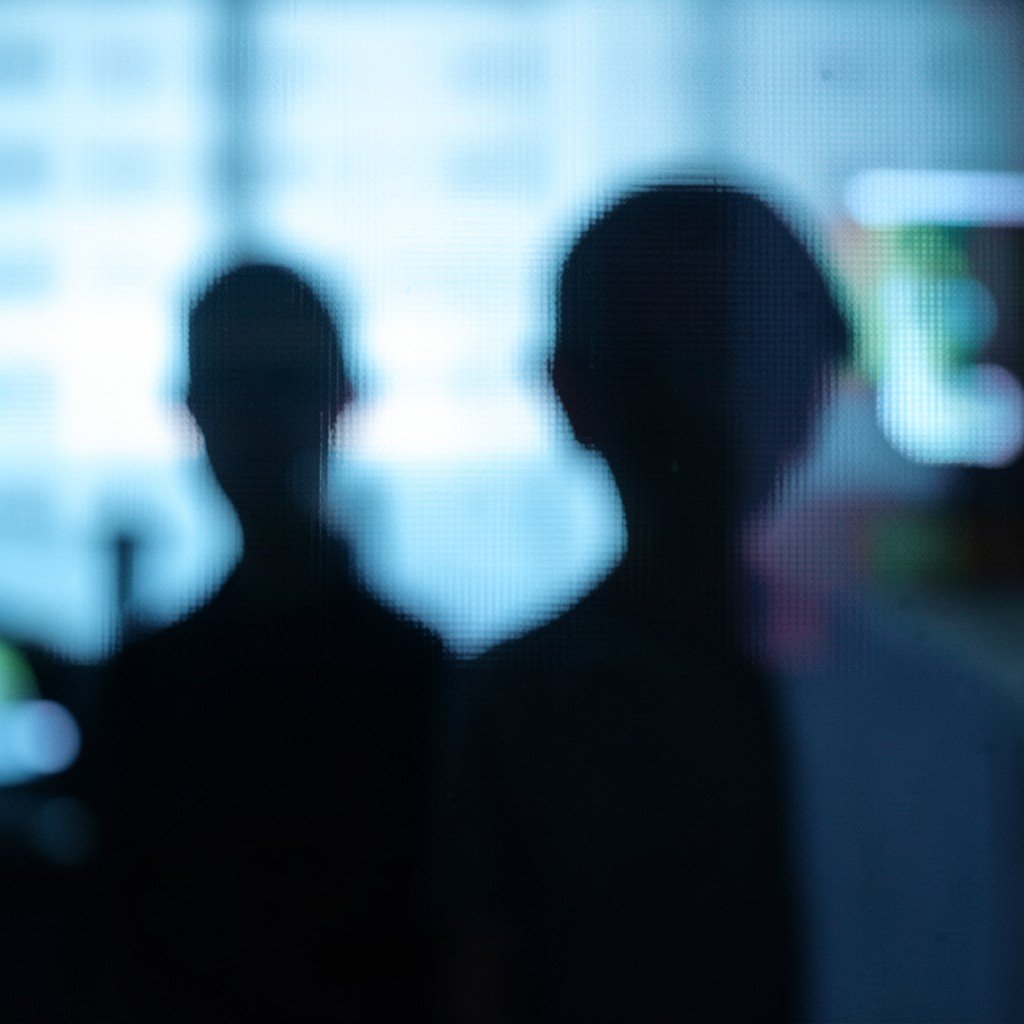 Close-up of a blurred digital screen reflection, human silhouette in the background, cool toned, depth of field, 16:9 ratio.