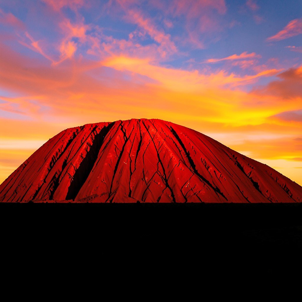 Uluru rock glowing in deep red and orange hues during sunset with a dark silhouette foreground, warm lighting, vivid sky, no text, 4:3